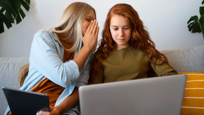 Dvě ženy šeptající si u notebooku