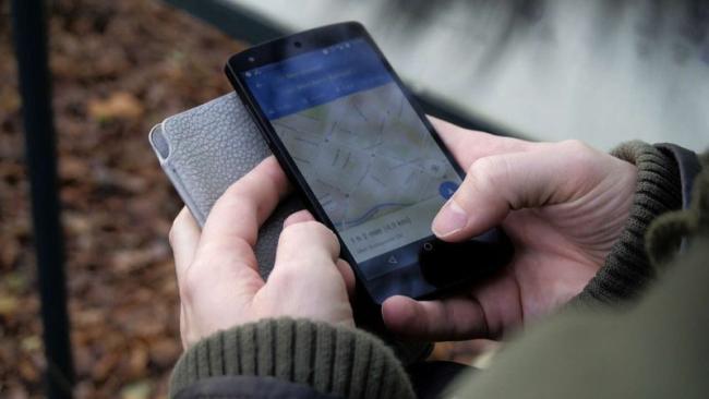 Smartphone v rukou uživatele, na displeji je aplikace Mapy Google
