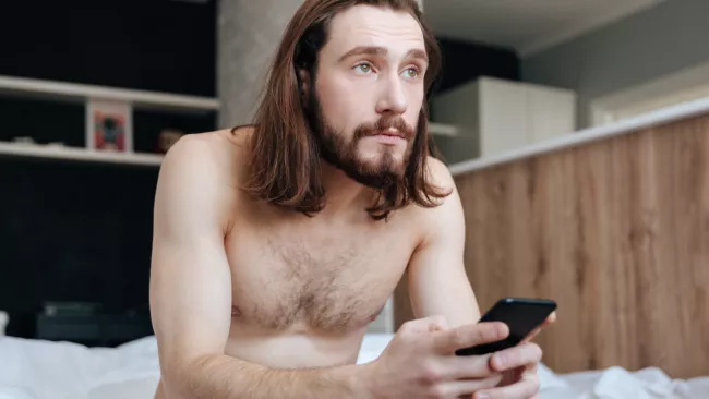 Nahý muž na posteli s telefonem