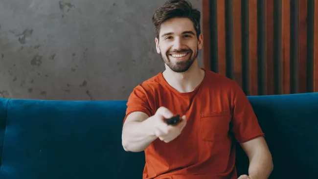 Mladý muž ovládá TV dálkovým ovladačem