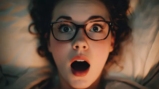 Šokovaná mladá žena ležící v posteli