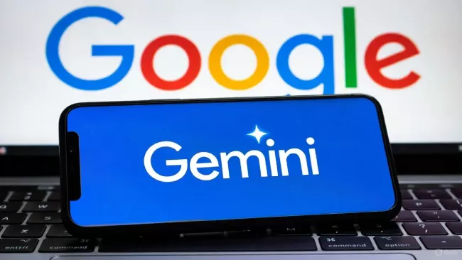 Laptop, na jeho klávesnici leží mobil, který má na displeji nápis Gemini