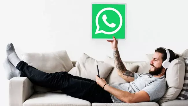 Muž leží na gauči a v ruce ukazuje ceduli s logem WhatsApp
