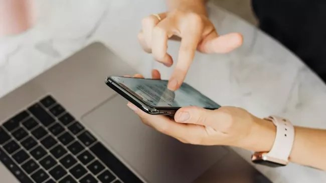Uživatelka pracuje s mobilem u klávesnice laptopu