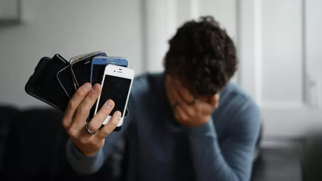 Zoufalý uživatel drží v ruce několik smartphonů