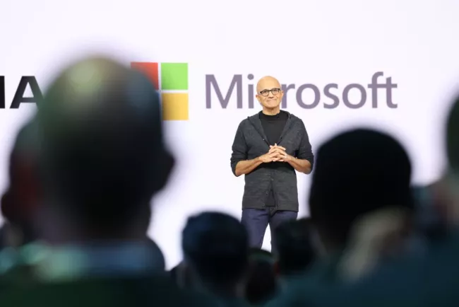 Satya Nadella stojící na pódiu před logem společnosti Microsoft.