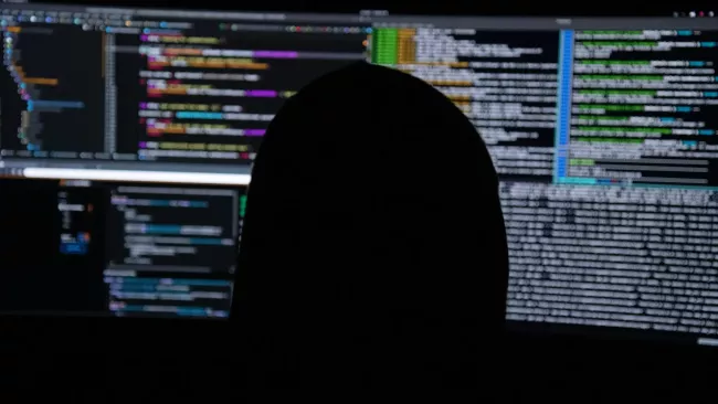 Hacker před monitory s kódem