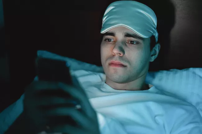 Člověk používá rozsvícený mobilní telefon v potemnělé místnosti před spaním.