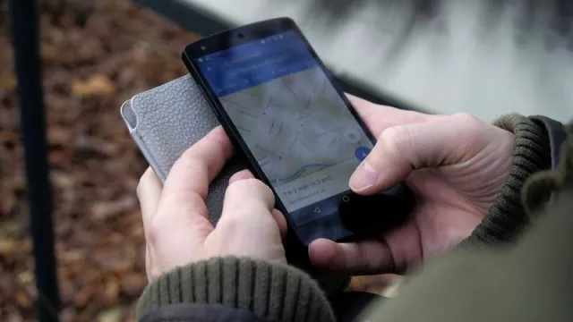 Smartphone v rukou uživatele, na displeji je aplikace Mapy Google