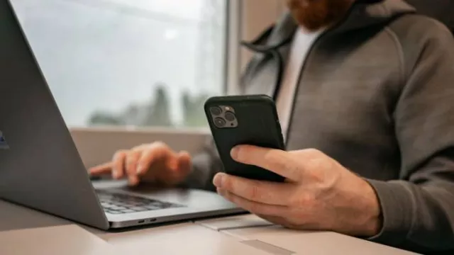 Muž u laptopu se smartphonem v ruce