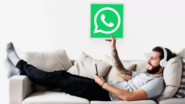 Muž leží na gauči a v ruce ukazuje ceduli s logem WhatsApp