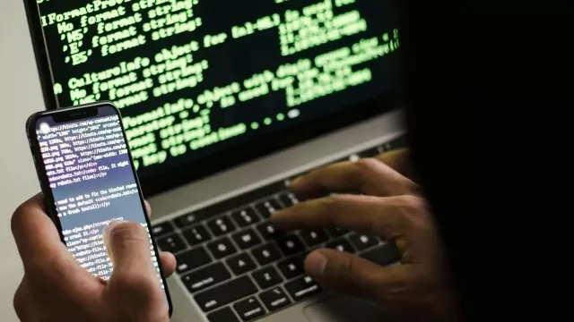 Hacker s mobilním telefonem a monitorem v pozadí