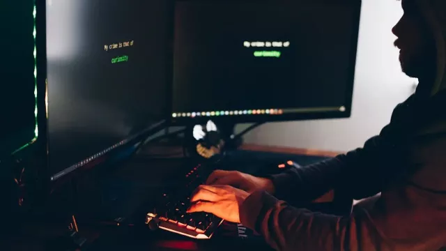 Hacker sedící v přítmí před dvěma monitory