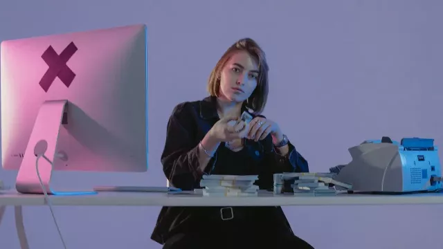 Mladá žena sedí u počítače a před sebou má hromadu peněz