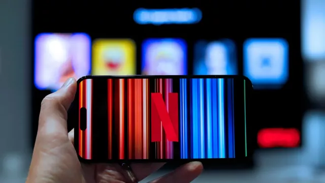 Logo Netflixu na displeji smartphonu a v pozadí je televizor