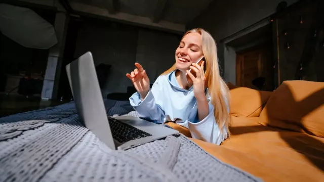 Mladá žena pracuje s laptopem a hovoří do smartphonu